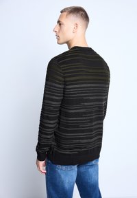 Black sweater with green and gray horizontal stripes, ribbed cuffs and hem, worn with blue denim jeans. View from the back.
