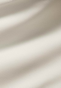 Texturerat tyg i ljus beige, med ett litet, upphöjt prickmönster. Slät yta med mjuka veck som visar ljus och skugga.