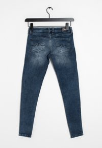 Tunna blå denimjeans med en urtvättad yta, som har två bakfickor med en vågig stickad design, hängande på en svart galge.