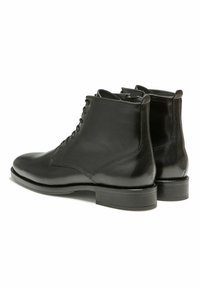 Bottines en cuir noir avec une finition lisse, bout rond, lacets à l'avant et un petit talon empilé. Détails de coutures sur les côtés.