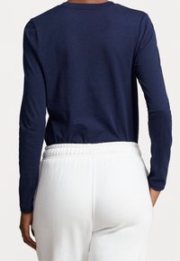 Marinblå långärmad tröja med rundad halsringning; matchad med vita, elastiska byxor. Slät tygkvalitet på båda plaggen.