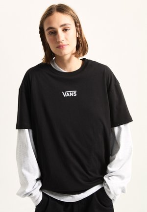Musta puuvillainen lyhythihainen t-paita, jossa on valkoinen "VANS"-logo. Kerroksittain harmaan pitkähihainen paidan päällä. Normaali istuvuus ja pyöreä kaula-aukko.