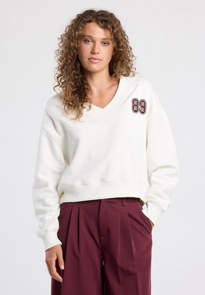 White sweatshirt with a V-neck and embroidered "89" detail in burgundy on the left chest. Soft material and relaxed fit.