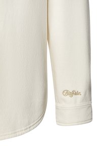 Cremefarbenes Langarmshirt aus weichem Stoff, mit abgerundetem Saum und einem goldenen gestickten "Buffalo"-Logo am Ärmel.