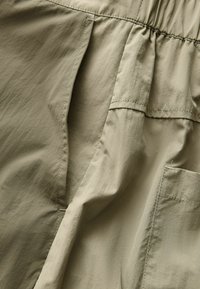 Nahaufnahme eines beigen Stoffes mit genähten Nähten, einem elastischen Bund und einer Tasche, die die Textur und Details der Kleidungsherstellung hervorhebt.