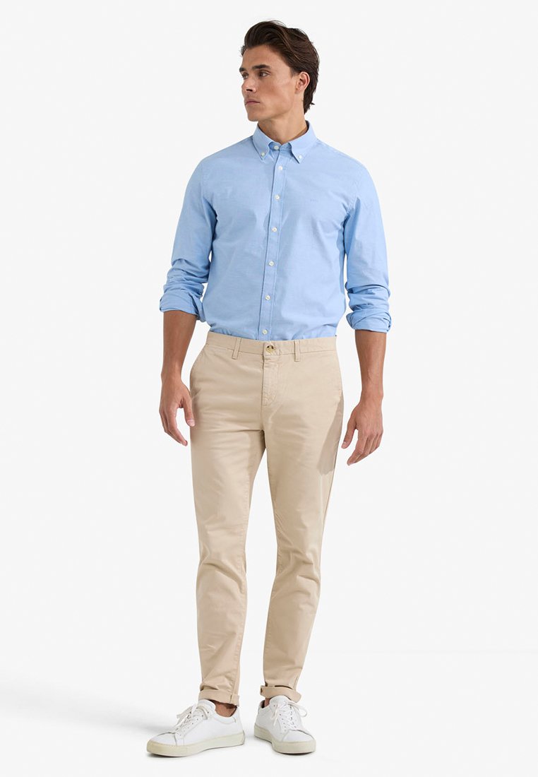 Jasnoniebieska, zapinana koszula, beżowe chinosy, białe trampki. Slim fit, bawełnowy materiał, podwinięte rękawy, jednolity design bez wzorów.