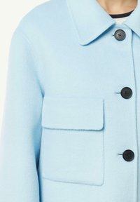 Giacca in misto lana azzurro chiaro con colletto, taschino sul petto e bottoni neri. Presenta una texture morbida e un design su misura.