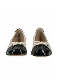 Ballerinas mit einer schwarzen Zehenkappe aus Lackleder, beigem Lederobermaterial und einer Schleifenverzierung mit Metallakzenten. Insgesamt glatte Textur.