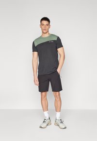 Herrtröja med kort ärm i grön överdel och mörkgrå nederdel. Matchas med svarta shorts och ljusa träningsskor.