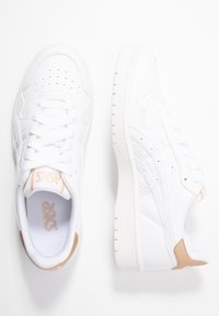 Weiße Sportsneaker mit einer strukturierten Lederoberfläche, perforierter Zehenpartie und hellbraunen Akzenten an Ferse und Zunge. Gummisohle.