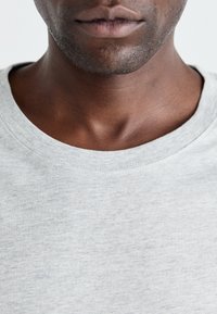 Grå t-shirt med rund hals lavet af blødt materiale, med en subtil tekstur og et simpelt design. Ingen synlige mønstre eller logoer.