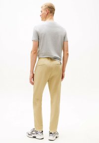 Chinos beige con cintura elástica, dos bolsillos traseros y un diseño ajustado, combinados con una camiseta de manga corta gris claro y zapatillas.