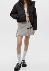 Svart puffjacka med cropped design, beige mini kjol med sidöppning och spänne, vita knähöga strumpor och svarta platåskor.