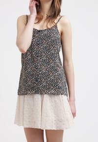 Květinový vzor na topu bez rukávů v černé barvě s růžovými a modrými květinami, doplněný o strukturovanou krémovou sukni s áčkovým střihem a vroubkovaným lemem.