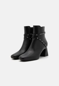 Black leather ankle boots with a square toe, chunky heel, and decorative strap featuring studs and logo at the ankle.
