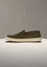 Chaki žalia lengvai užsimaunama avalynė su balta padais, mažo profilio, su mažomis daugiaplėtinėmis dryžuotomis audinio detalėmis prie kulno.