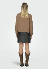 Maglione marrone testurizzato, mini gonna in pelle nera e stivali da cowboy color beige. Modella vista di spalle, che mette in risalto il look a strati dell'outfit.