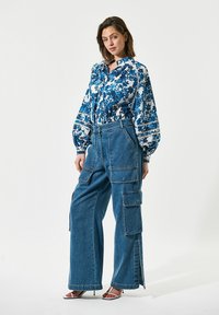 Bloemmotief blouse in blauw en wit met puff sleeves, gecombineerd met high-waisted, wijde denim cargo broeken met meerdere zakken.