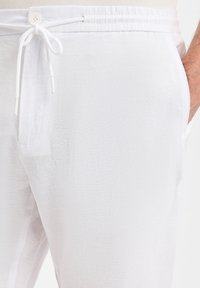 Weiße Leinenhose mit Kordelzugbund, einer seitlichen Tasche und strukturiertem Stoff für leichten Komfort.