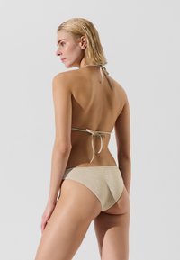 Bikini set v jemně béžové barvě s lesklým povrchem. Design s halter krkem a nastavitelnými tkaničkami; bikini spodní díl má hladký, minimalistický styl.