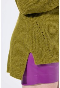 Maglione a maglia verde oliva con texture a coste e spacchi laterali, indossato su pantaloni corti in pelle viola lucida. Presenta una vestibilità rilassata e un motivo distintivo.