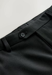 Mustad püksid tekstuurse viimistlusega, mis sulguvad nööpide ja luku kaudu ning millel on vööaugud vöökoha ümber.