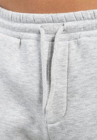 Hellgraue Sweatpants mit elastischem Bund, Kordelzug und Seitentaschen. Der Stoff hat eine weiche, strukturierte Oberfläche.