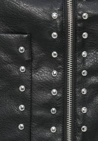 Μαύρο δερμάτινο μπουφάν με ασημένιες τρουκς και κεντρικό φερμουάρ. Η υφή είναι λεία με απαλό κόκκο, τσέπη στην αριστερή πλευρά.