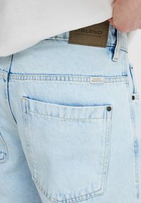 Lichtblauwe denim shorts met een leren merkpatch, voorzien van een achterzak met een klein label en minimale stikdetails.