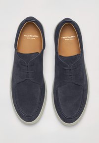 Sneakers in suede blu navy con punta tonda, lacci e suola beige. L'interno presenta una soletta color cammello con l'etichetta "FRED MARTIN MADE IN SPAIN."