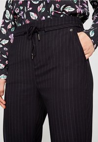 Pantaloni a righe nere con vita regolabile tramite cordino, tasche laterali e una texture di tessuto liscia. Accentuati da un piccolo dettaglio con logo.