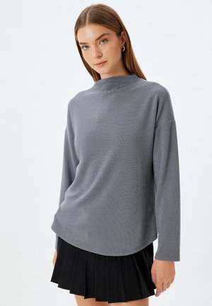 Grijze langemouwen top met hoge hals, textuurstof, relaxte pasvorm en afgeronde zoom, gecombineerd met een zwarte plissé rok.