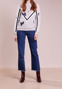 Felpa grigia con ricami floreali, design a zig-zag e strisce nere. Abbinata a jeans blu e stivali alla caviglia bordeaux.