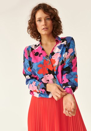 Colorful long-sleeve blouse featuring a floral pattern in pink, blue, and red tones, paired with a pleated red skirt.