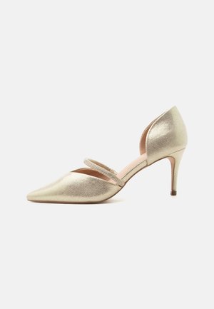 Gouden pumps met spitse neus en een dun enkelbandje versierd met kleine strass-steentjes, afgebeeld op een witte achtergrond.