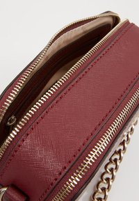 Burgunderrotes Lederhandtasche mit zwei Reißverschlussfächern, goldfarbenen Beschlägen, strukturiertem Oberflächen und dekorativem Kettenriemen.