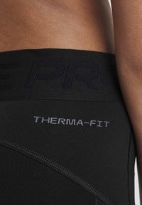 Leggings neri Therma-Fit con una fascia ampia in vita, caratterizzati da un marchio in rilievo e dettagli cuciti, che mostrano una texture liscia ed elastica.