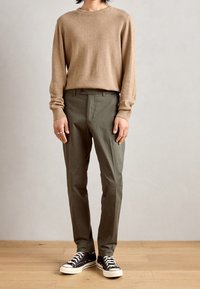 Beige ulltröja, olivgröna byxor och svarta sneakers med vita sulor. Byxorna har flat front och sidofickor.