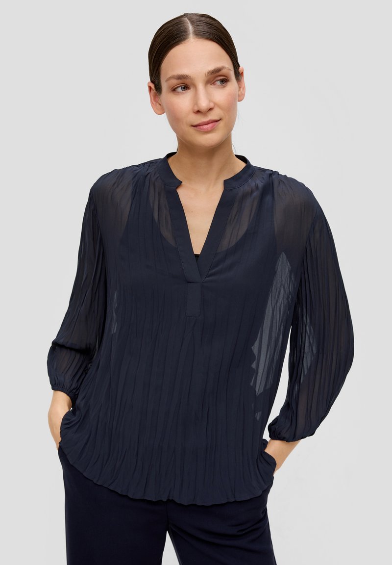 Navy blauwe geplooide blouse met een V-hals, lange mouwen en geplooide manchetten, gemaakt van lichtgewicht, transparante stof. Subtiele textuur en vloeiende uitstraling.