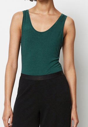 Dark green tank top in soft fabric, featuring wide straps and a scoop neckline. Paired with black high-waisted trousers.