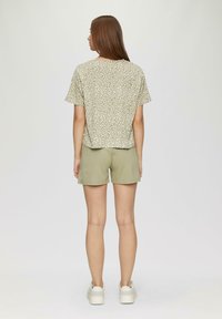 Bluzka z krótkim rękawem w jasnym zielonym kolorze, pokryta białym nakropkowanym wzorem, w połączeniu z pasującymi zielonymi szortami. Model stoi z widoczną plecami.