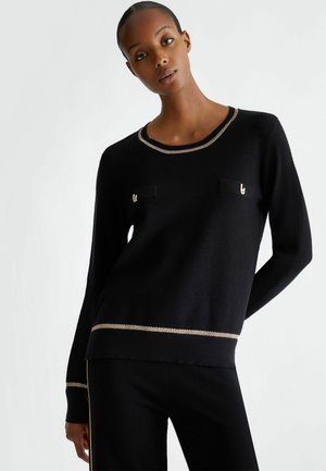 Maglione nero a maglia con collo rotondo, accenti di filo dorato e due tasche sul petto. Presenta un tessuto testurizzato e una vestibilità leggermente larga.