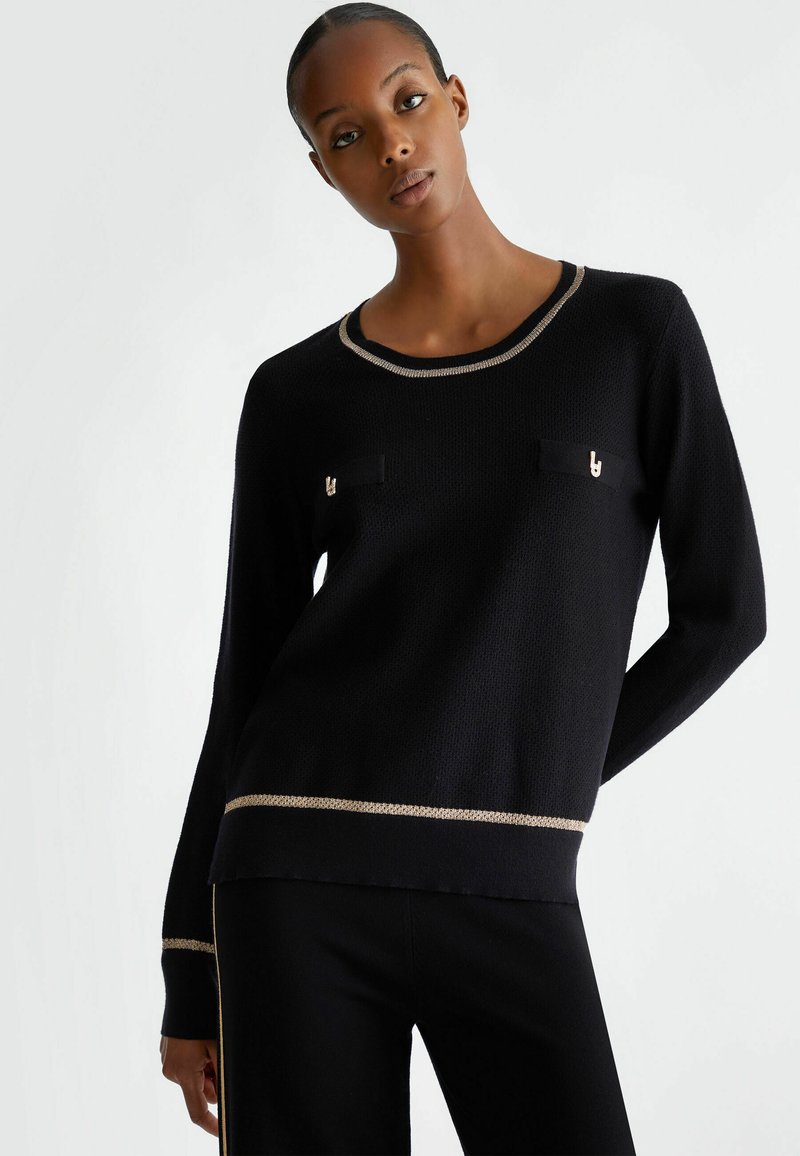 Maglione nero a maglia con collo rotondo, accenti di filo dorato e due tasche sul petto. Presenta un tessuto testurizzato e una vestibilità leggermente larga.