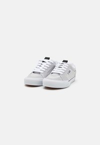 Pantofi sport gri din suede cu sireturi albe și tălpi din cauciuc. Au un tab-ul din spate negru și un branding subtil pe lateral. Formă clasică de tip low-top.