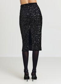 Schwarzer Bleistiftrock mit Pailletten und einem Schlitz auf der Rückseite. Glatte Textur mit glänzenden Akzenten. Kombiniert mit schwarzen Strumpfhosen und offenen, hochhackigen Schuhen.