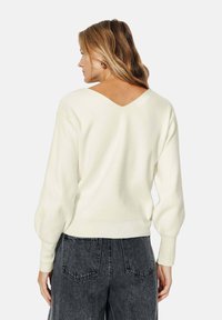 Pull oversized crème clair avec un dos en V, des poignets et une ceinture côtelés, associé à un jean foncé taille haute.