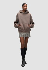Brown oversized hoodie with a kangaroo pocket, paired with a grey herringbone skirt and black knee-high socks, complemented by black ankle boots.