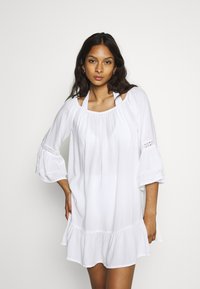 Vestido blanco de corte holgado con mangas acampanadas, que presenta un dobladillo con volantes y detalles de encaje en las aberturas de las mangas. Tela suave y ligera.