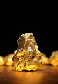 Gouden klomp met een ruwe, gestructureerde oppervlakte. Bevat glanzende, metalen tinten en gekartelde randen, geplaatst tegen een donkere achtergrond.