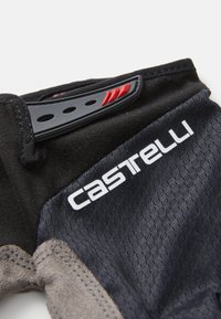 Mănușă de ciclism neagră, cu un material texturat de culoare neagră, accente gri și un detaliu de curea roșie și neagră. Include un logo alb pe lateral.